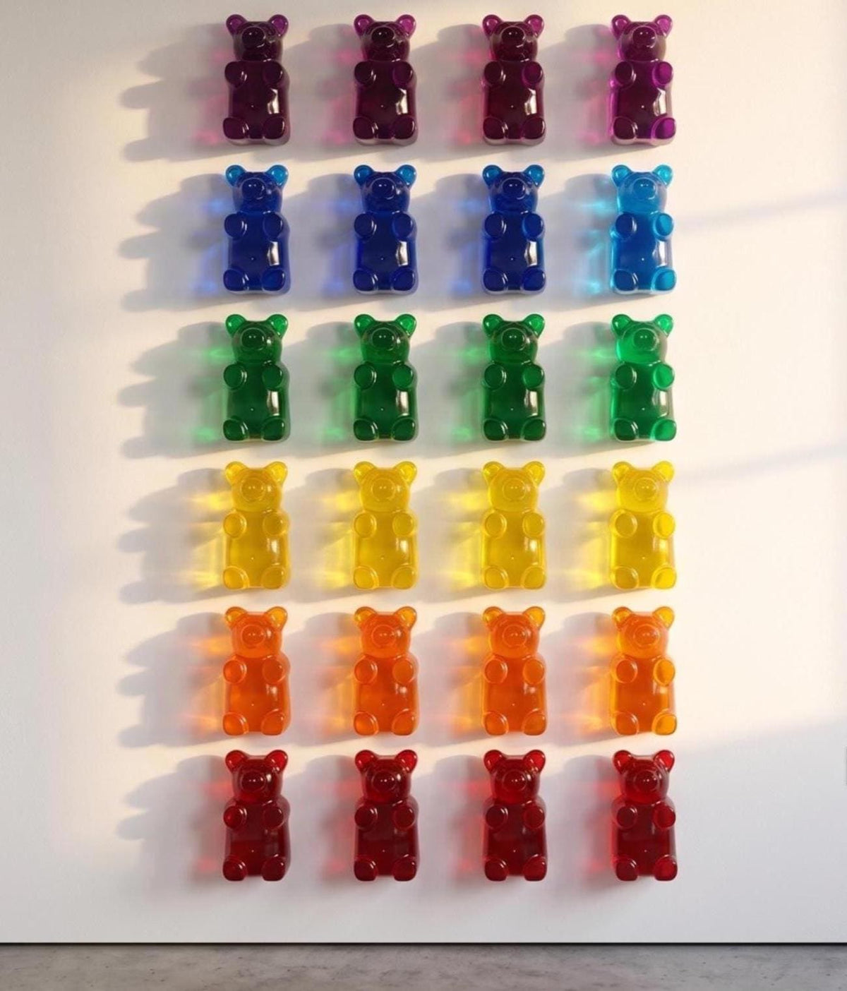 A professional art installation on a bright white wall featuring twenty-four 7-inch translucent gummy bear sculptures